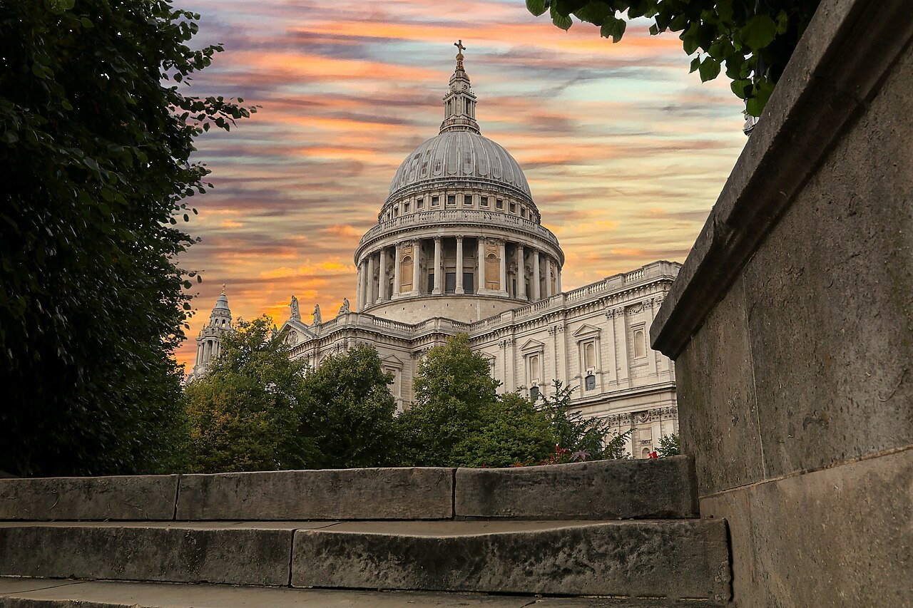 St Paul's dome at sunset, its drum and colonnade seen past a wall under a pink sky
