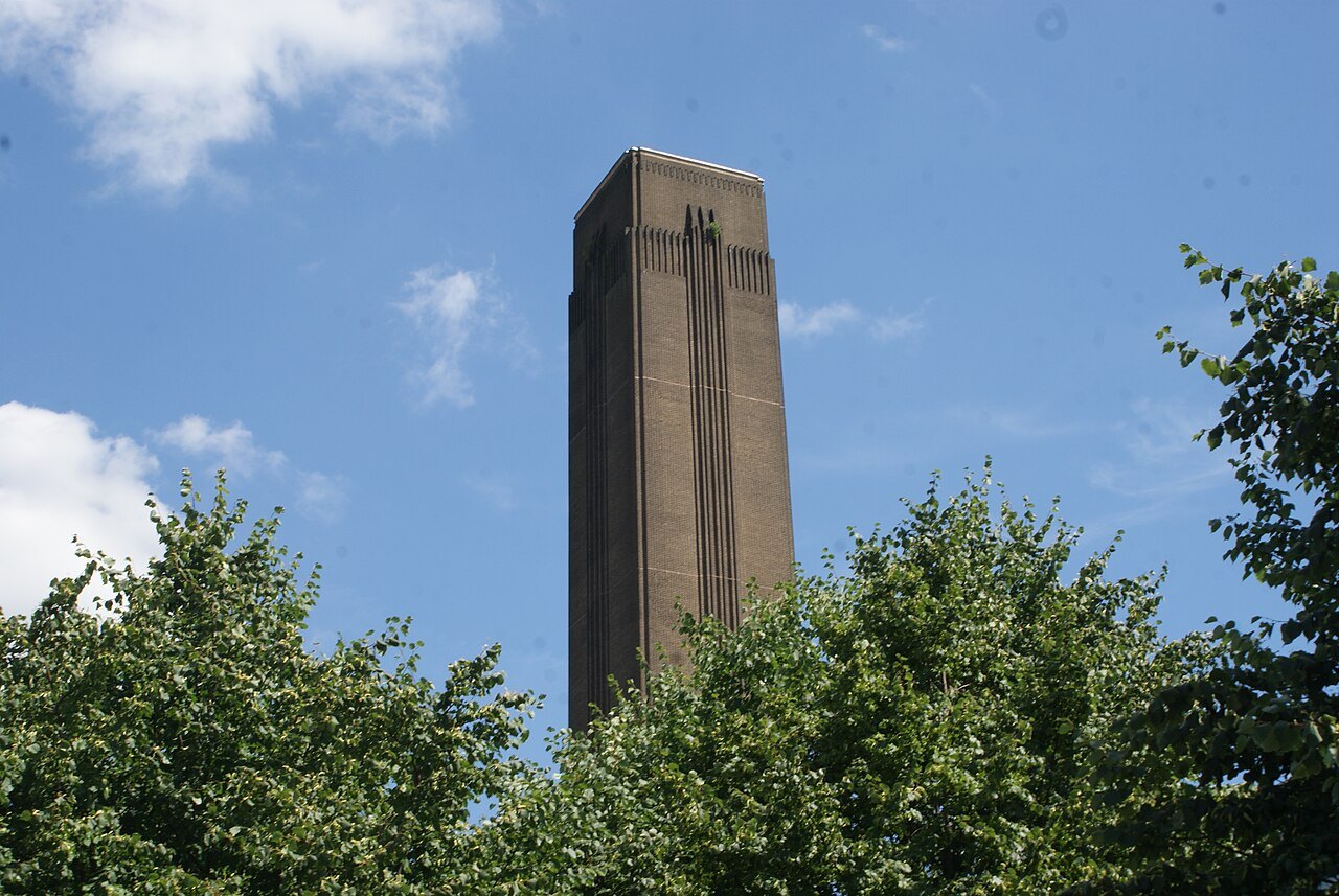 The square brick chimney of Tate Modern rising above trees against a blue sky