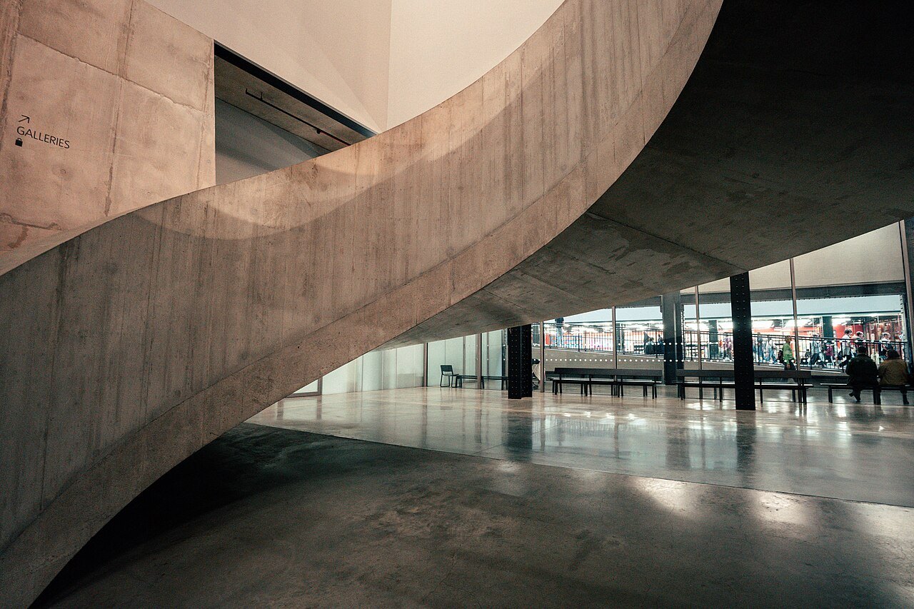 A sweeping concrete spiral stair in the new building at Tate Modern, with a glazed floor below