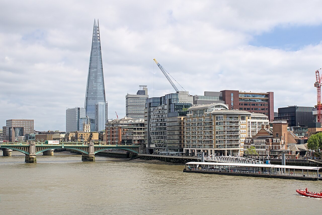 The Shard beyond the riverside buildings, seen from the river with a bridge and cranes