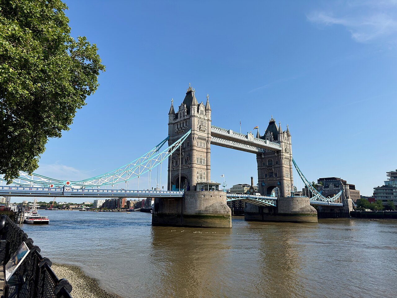 Tower Bridge and its blue suspension chains from the north bank, with a path along the wall
