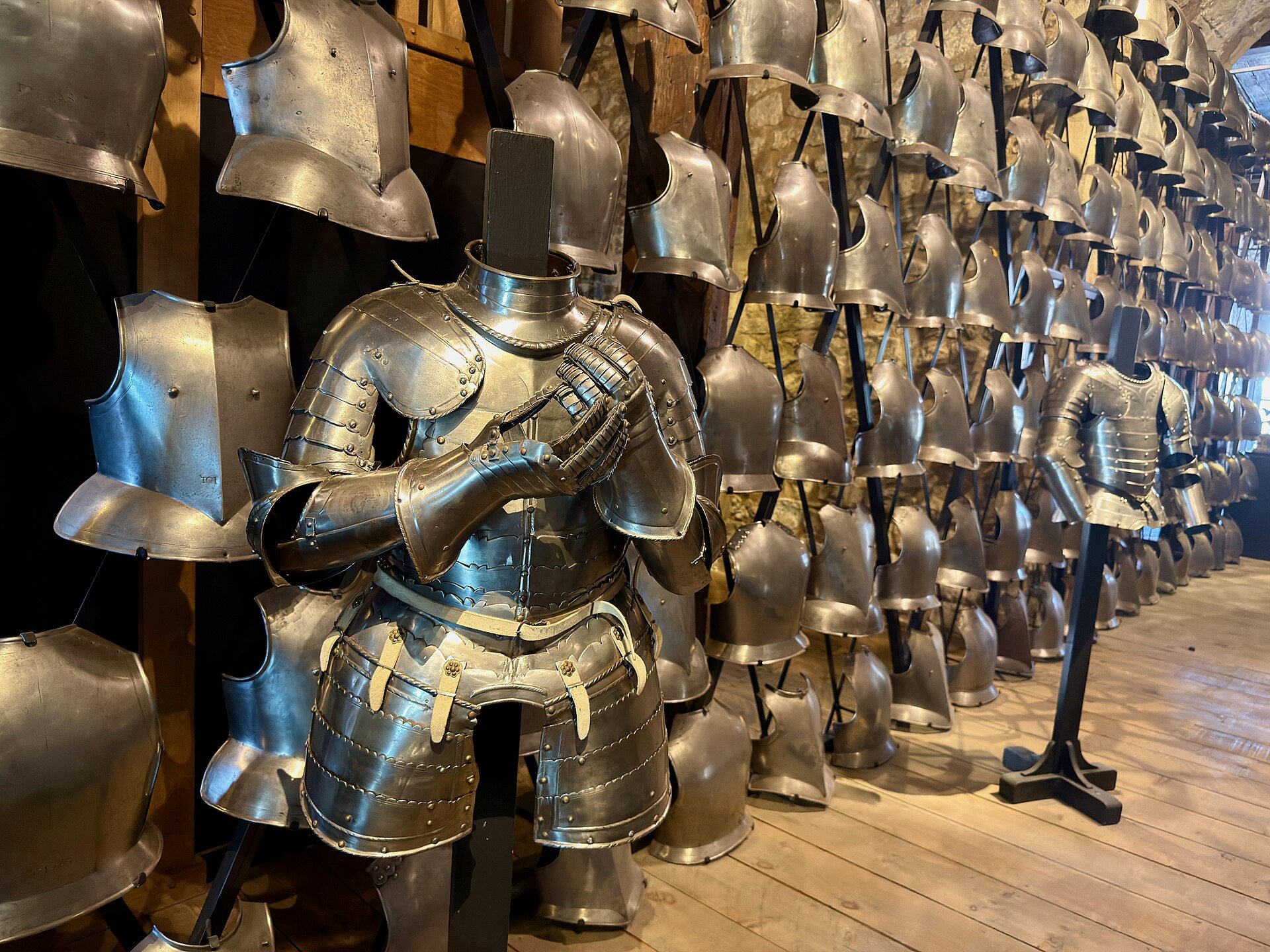 Rows of steel armour on stands in an exhibition at the Tower of London, an armoured figure in front