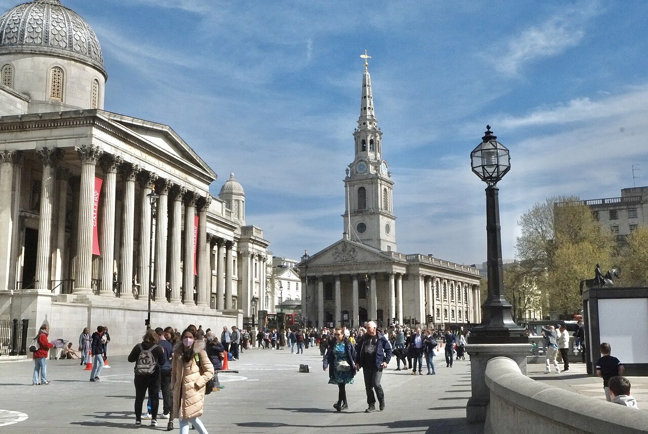 The National Gallery and St Martin-in-the-Fields across Trafalgar Square on a bright day, with people crossing