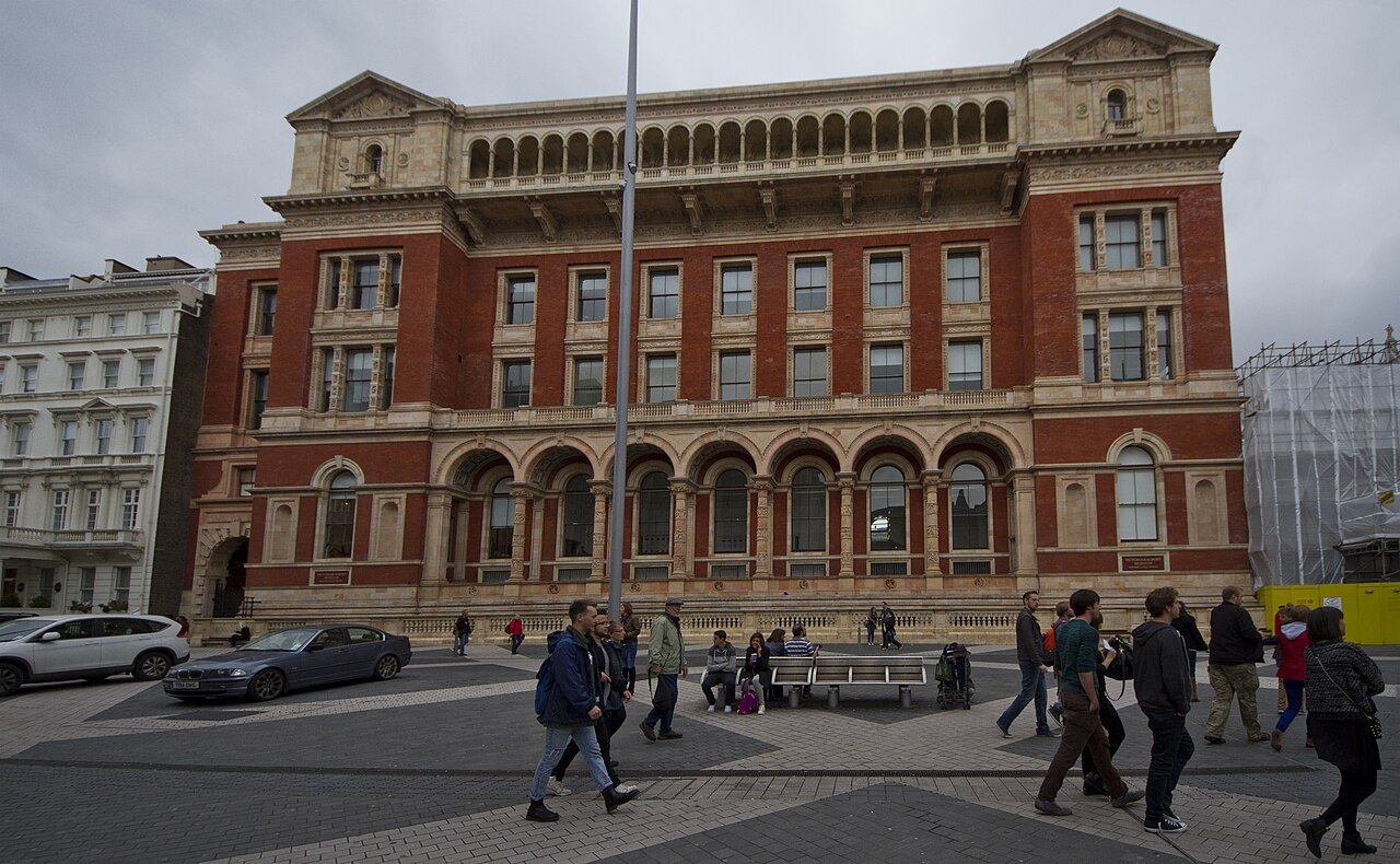 The red brick and terracotta front of the Victoria and Albert Museum, with people crossing the street in front