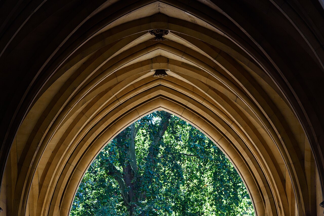A pointed stone arch framing green leaves, in the entrance to the abbey's precinct