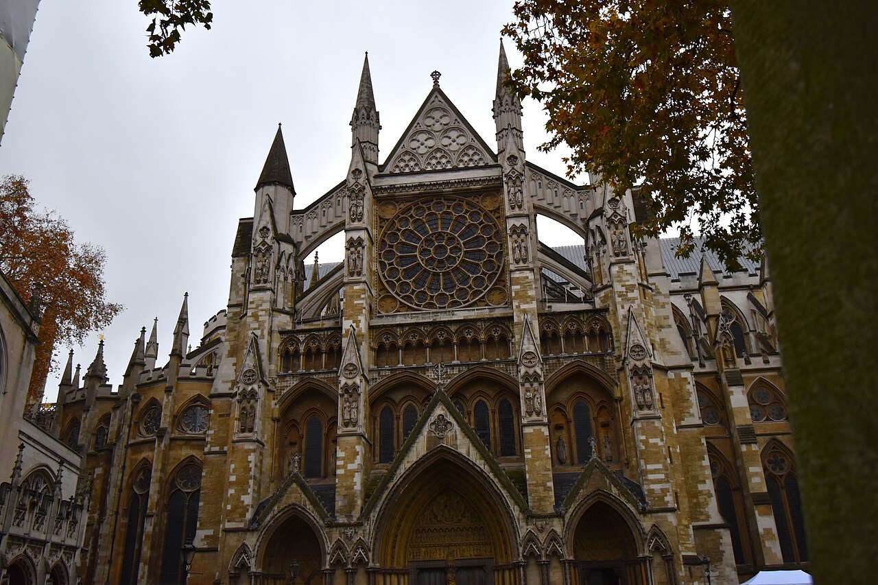 The great rose window and gabled porch of the abbey's north transept, seen from below through autumn leaves