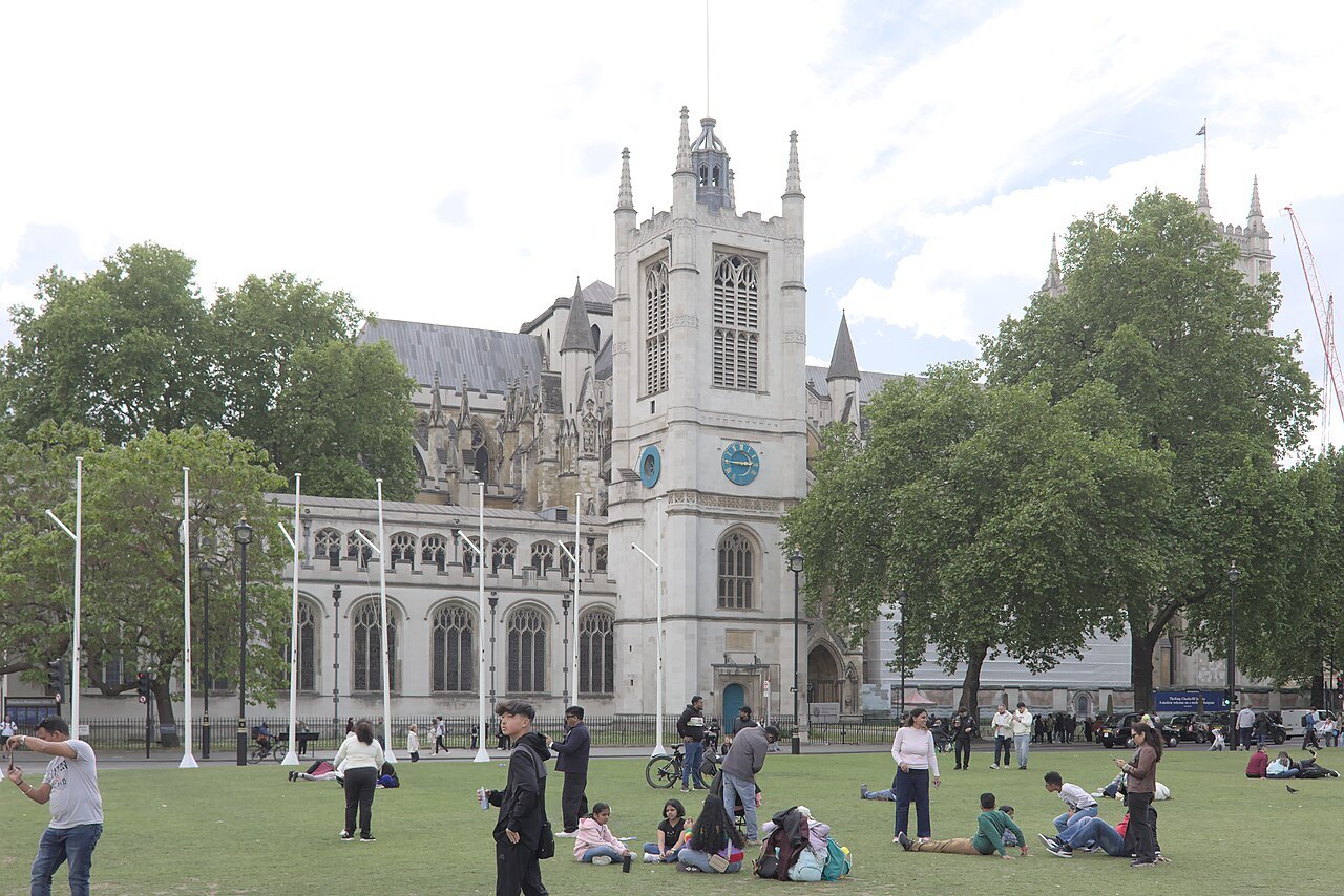 People on the lawn with a church tower and the north side of Westminster Abbey behind them
